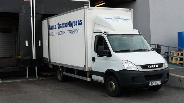 En hvit lastebil fra Iveco med påskrift for transport og logistikk, parkert ved en lastebrygge.