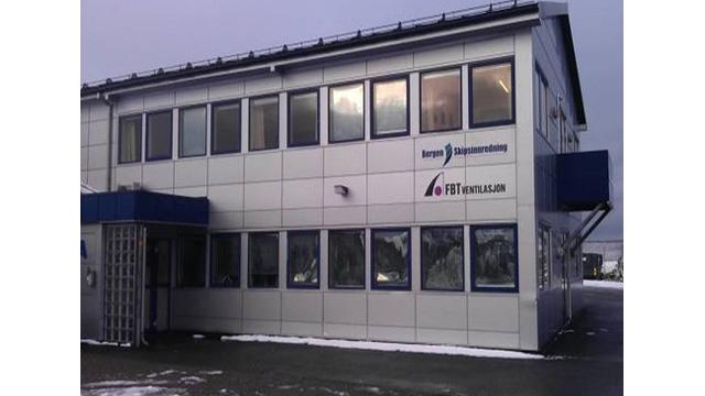 Moderne kontorbygg med mange vinduer og logoen til et selskap på fasaden. Snø på bakken.