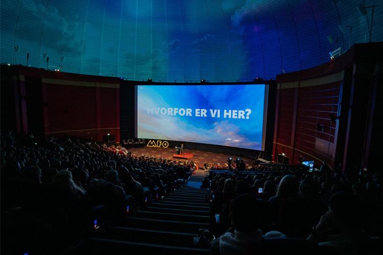 En fullsatt kinosal med et stort lerret som viser teksten "HVORFOR ER VI HER?" under en filmvisning.