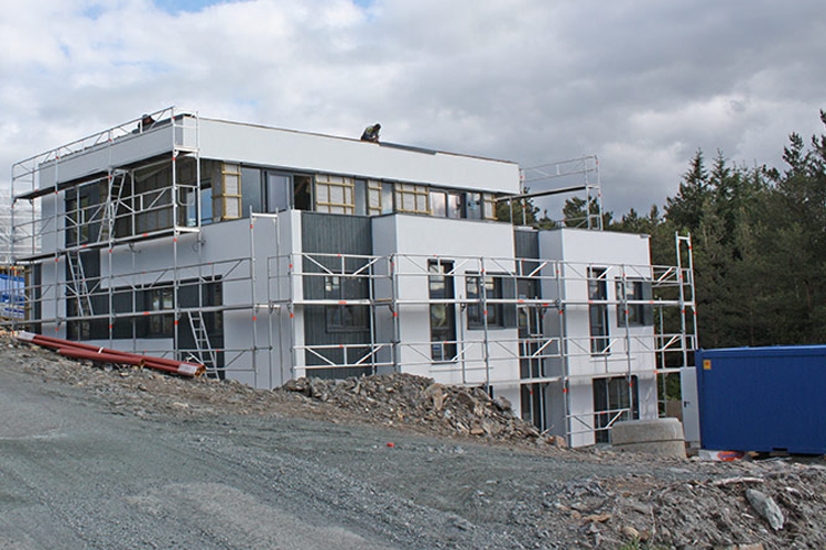 Moderne bygning under konstruksjon med stillas og grusvei i forgrunnen.