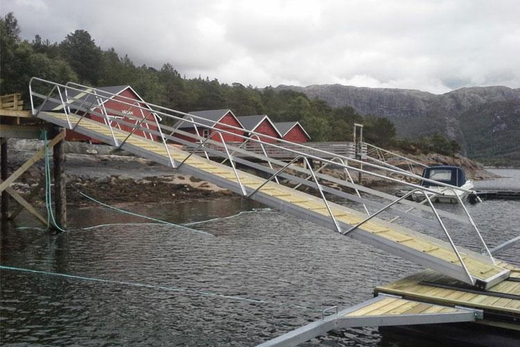 Bilde av en rampe som fører ned til vannet, med røde hytter i bakgrunnen og fjell i horisonten.