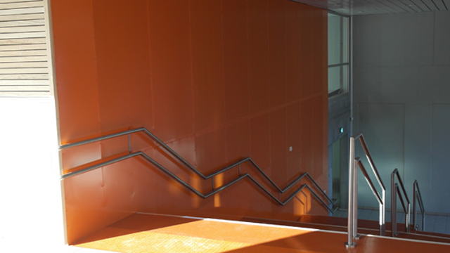 Trappen med oransje vegger og metallrekkverk som fører nedover i en moderne bygning.