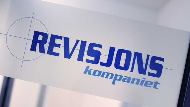 Revisjonsfirmaets logo på glassdør med teksten "REVISJONS kompaniet" i blått.