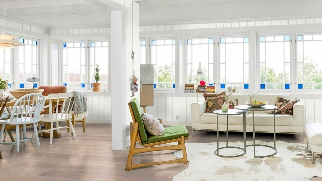 Lyst og moderne stue med hvite vegger, store vinduer, en sofa, stoler og et spisebord i en åpen planløsning.