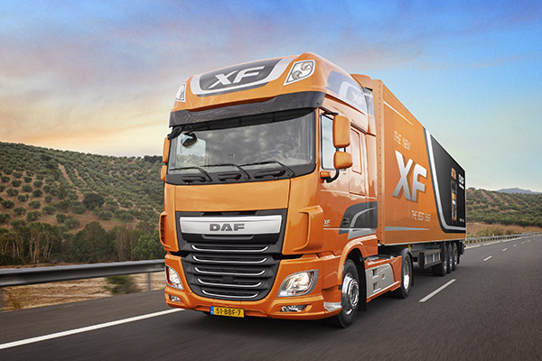 En oransje DAF XF lastebil kjører på en vei med grønne åser i bakgrunnen.