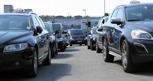 Kø med svarte biler og taxier på en parkeringsplass i byen.