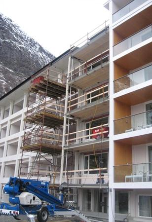 Bygning med stillas og heis under renovering, omgitt av fjell og snø.