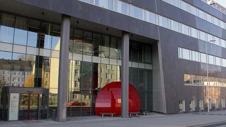 Moderne kontorbygg med glassfasade og en stor rød inngang ved foten av bygningen.