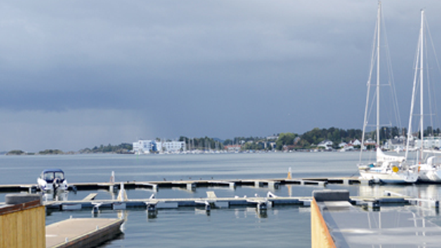 Utsikt over en marina med båter og seilbåter, under en mørk himmel med truende skyer.