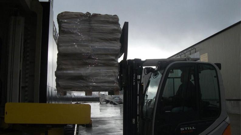 Gaffeltruck løfter en pall med pakker ved en lagerbygning under overskyet vær.