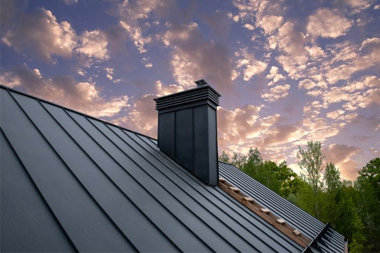 Tak med metallbelegg og pipe mot en fargerik himmel med skyer og trær i bakgrunnen.