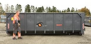 En arbeidstaker i arbeidsklær går forbi en stor grå container på en byggeplass.