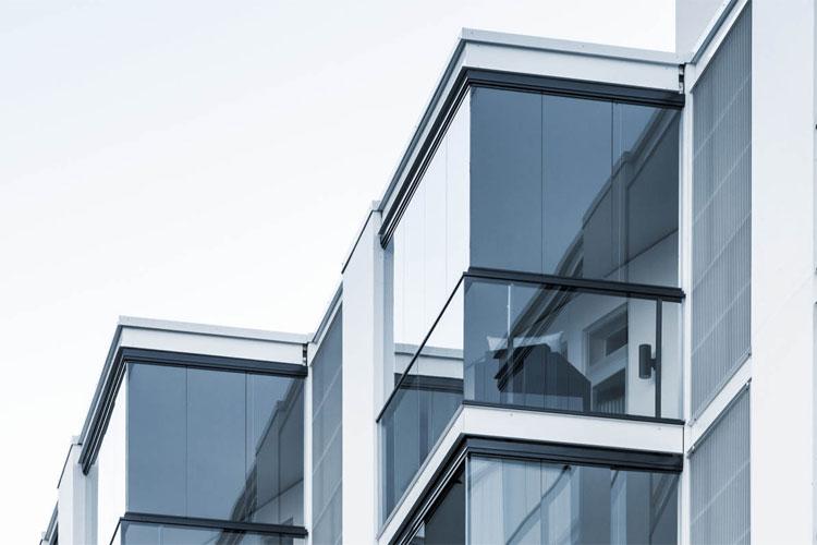 Moderne leilighetsbygg med store vinduer og balkonger i glass. Arkitektonisk design med minimalistisk stil.