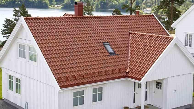 Moderne, hvitt hus med rød takstein og vindu, beliggende ved vannet i naturskjønt område.