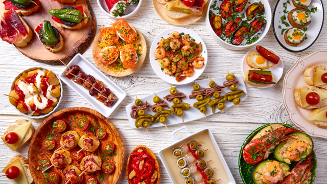 Et variert utvalg av tapasretter, inkludert reker, oliven, skinker, og fylt paprika på et bord.