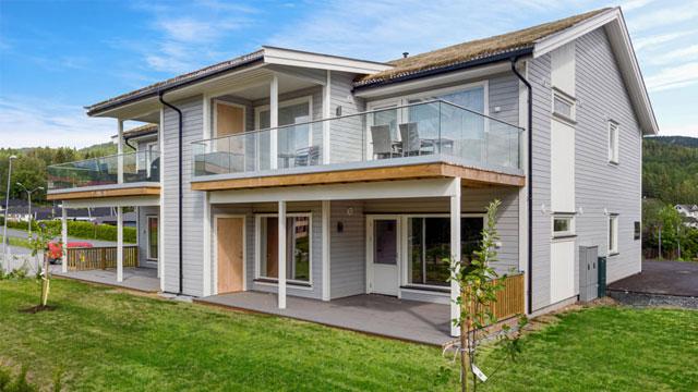 Moderne enebolig med balkonger, stor hage og glassrekkverk, omgitt av grønt landskap.