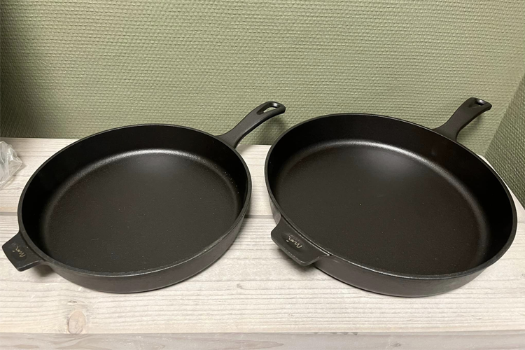 To store og stekepanner i svart støpejern på en lys treoverflate.