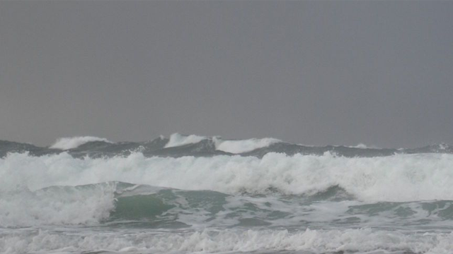 Bølger som slår mot stranden under en grå himmel med mørke skyer.