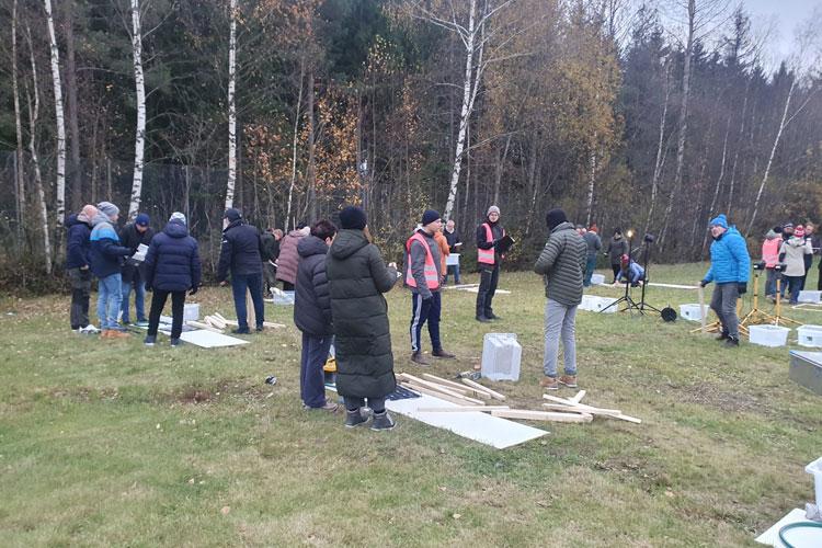 En gruppe mennesker deltar i en utendørs aktivitet i skogen, med materialer og utstyr rundt seg.