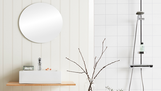 Moderne bad med rund speil, hvit servant på trehyll, og dusj med minimalistisk design.