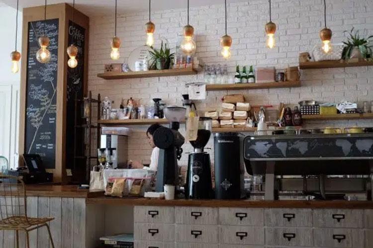 Kaféinteriør med en barista som lager kaffe bak disken, hyller med mat og drikke, og stilige lamper.