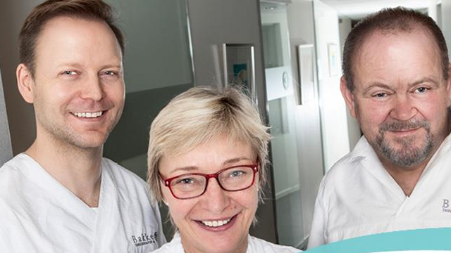 Tre smilende helsearbeidere i hvite frakker står sammen i en moderne klinikk.