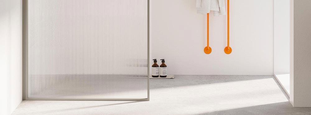 Moderne interiør med glassdør, oransje detaljer og to flasker på gulvet i et lyst rom.