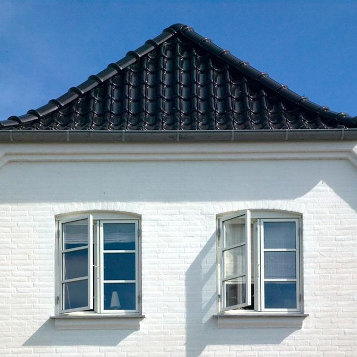 Hvitt hus med to åpne vinduer og svart tak, mot en klar blå himmel.