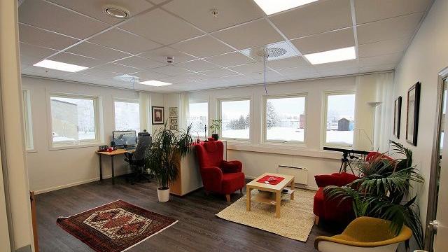 Lyst kontor med to røde stoler, et skrivebord med datamaskin og planter i vinduskarmen.