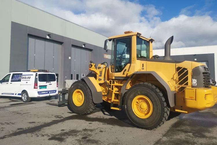 En stor hjullaster i gult står parkert foran en bygning, med en servicebil i bakgrunnen.