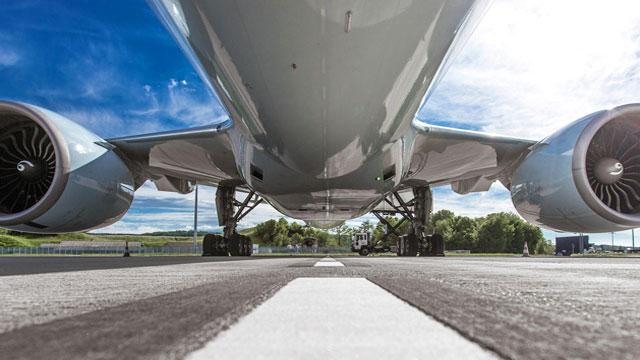 Bilde av en flymotor sett fra bakkenivå, med en klar blå himmel og rullebanen i forgrunnen.