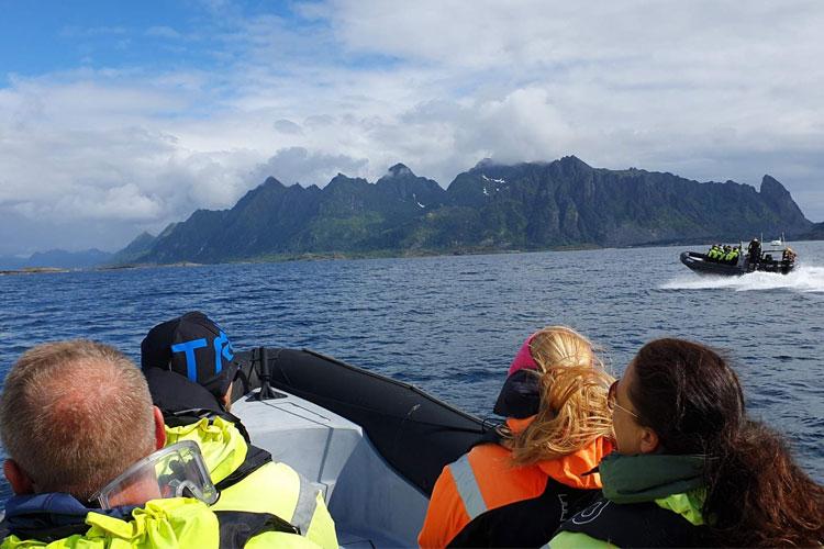 Folk i en båt med fjell i bakgrunnen, på en solfylt dag i Lofoten, Norge.