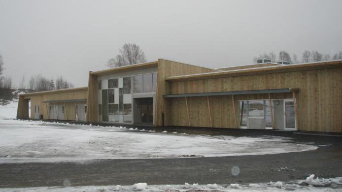 Moderne trebygning med store vinduer, beliggende i snødekt landskap.