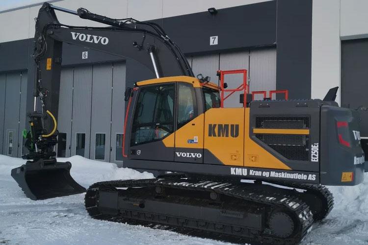 Gravemaskin fra Volvo med belter og snøskuffe, parkert foran en bygning i snødekt landskap.