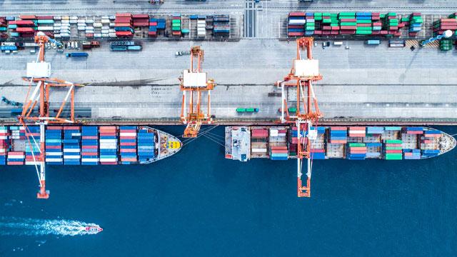 Oversiktsbilde av en havn med containere og fraktskip som laster og losser varer.