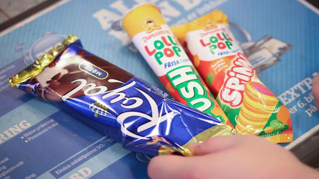 En hånd holder tre forskjellige iskremer: en sjokoladeis, en lollipop og en fargerik spiralis.