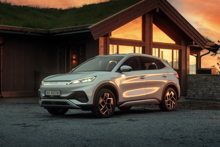 En sølvfarget SUV parkert foran en hytte med solnedgang i bakgrunnen.