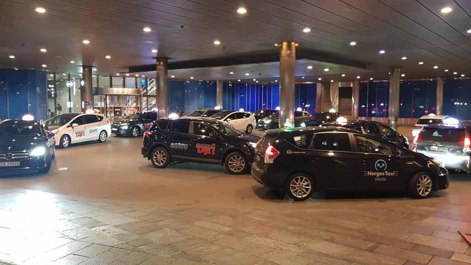 Taxis parkert foran en moderne bygning med lys og glassfasade om kvelden.