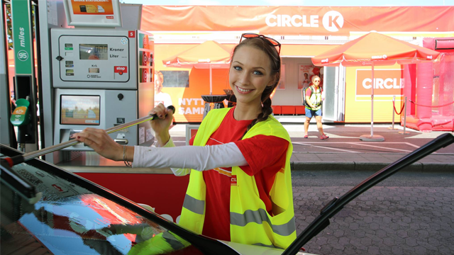 Kvinne i gul vest vasker frontruten på en bil ved en Circle K bensinstasjon.