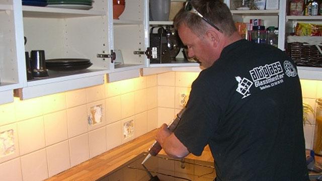 En håndverker jobber med å installere en benkeplate på kjøkkenet, med skap og belysning i bakgrunnen.