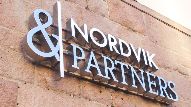 Skilt med teksten "& NORDVIK PARTNERS" på en murvegg, med moderne skrifttype og lys blå farge.