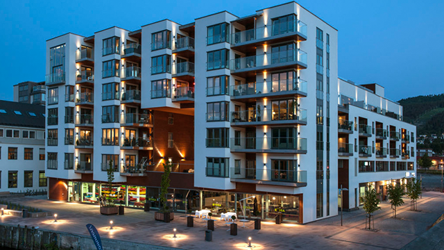 Moderne leilighetskompleks ved havnen, opplyst om kvelden med balkonger og uteplasser.