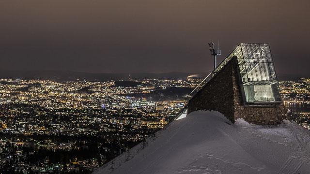 Utsikt over en snødekt by med lys fra bygninger og fjelltoppen i forgrunnen.