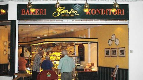 Bakeri og konditori med kunder som ser på bakervarer i en koselig butikk.