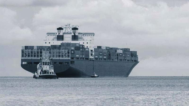 Containerfartøy med mange kasser ligger til kai, mens en slepebåt navigerer i nærheten.