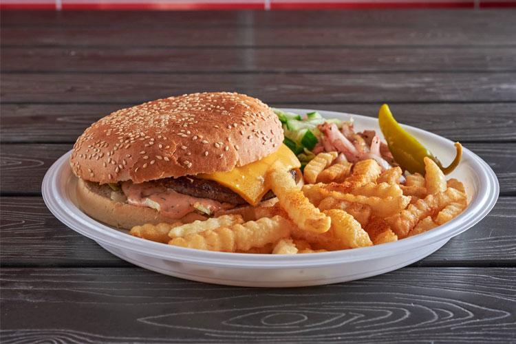 En sesambrød hamburger med ost, sprø pommes frites, salat og syltet agurk på en hvit tallerken.