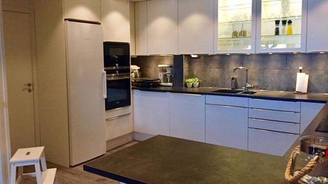 Moderne kjøkken med hvite skap, svart benkeplate, ovn, oppvaskmaskin og grønne planter på benken.