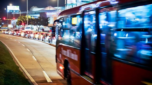 En rød buss kjører forbi i en travel gate med bilkøer og lys om natten.