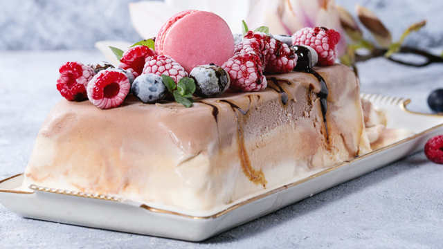 En delikat iskake med bær, sjokolade og en rosa makron på toppen, ser fristende ut på et fat.