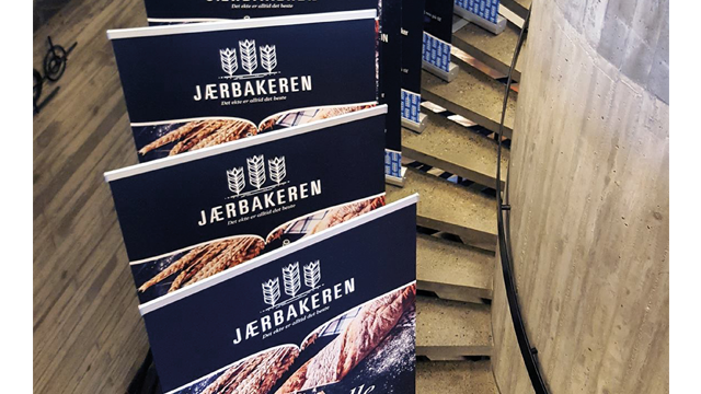 Stående bannere med Jærbakeren-logo og brødmotiv plassert langs en spiraltrapp i moderne interiør.